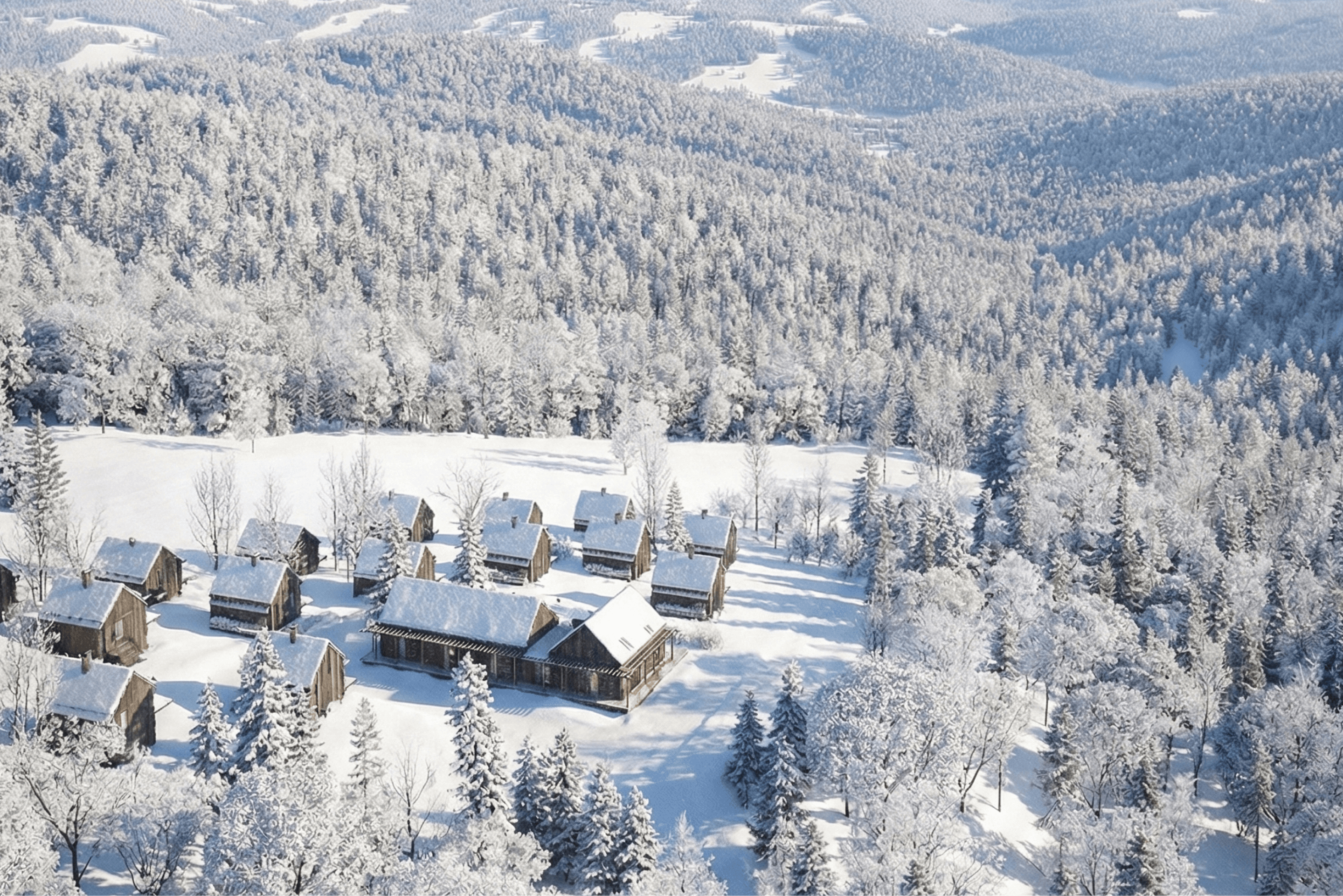 Vzdálený pohled na moderní chaty zasazené v lese s kopcovitou krajinou v pozadí.